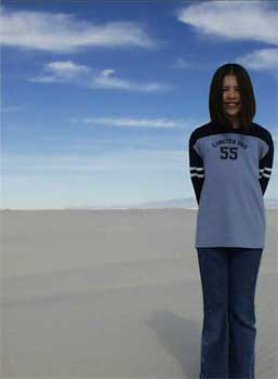 Jennifer Ann Crecente, a teenage girl with shoulder-length hair, is wearing jeans and a long-sleeve shirt. Jennifer smiles for the camera. Above her are rich blue skies with scattered clouds. The sky is similar to the processed header image of sky, clouds, and sun at the top of this web page. Beneath Jennifer are gypsum sand dunes. Jennifer's shadow is cast a short distance behind her across the undulating waves of sand. The sky and sand continue to the horizon, meeting near the midpoint of the photo. Photograph taken at White Sands National Park in New Mexico.